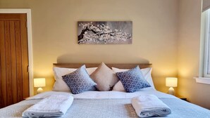 A neatly made bed with patterned bedding and pillows, a wall-mounted artwork, and bedside lamps. - Muirton Cottage - Rural Bliss (Angus)
