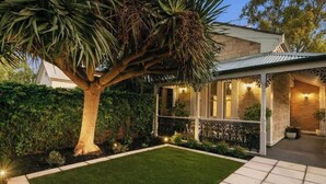 Een modern huis met een verzorgde tuin, een grote boom en een overdekt terras met verlichting.