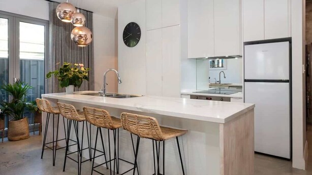 Een moderne keuken met een centraal eiland, barstoelen, een koelkast en een klok aan de muur.