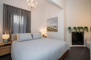A bedroom with a large bed, a chandelier, a painting, and a fireplace with plants. - 3 bedroom renovated 1890s Villa (Parkside)