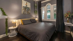 Een slaapkamer met een groot bed, een kroonluchter, een schilderij en een raam met gordijnen.