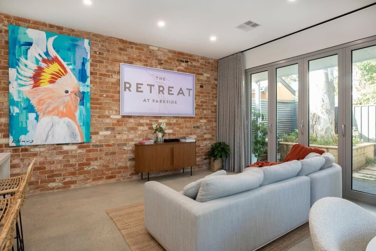A modern living room with a large sofa, a coffee table, a painting of a bird, a sign reading 'The Retreat at Parkside,' and a glass door leading to an outdoor area.