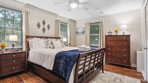 Une chambre à coucher avec un lit en bois, une table de chevet avec une lampe, une commode et un ventilateur de plafond.