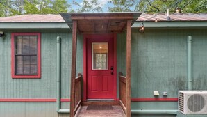 Un petit bâtiment d’un seul étage, avec une porte rouge et une véranda en bois.