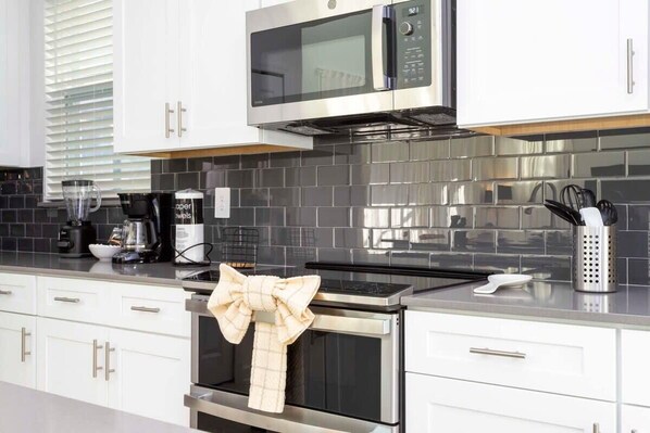A modern kitchen with white cabinets, a stainless steel microwave, and a black tiled backsplash.