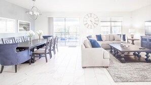 A spacious living room with a dining area, a sofa set, a coffee table, and a TV. - Champions Gate 8BR Villa-pool Game Room Theater (Davenport)