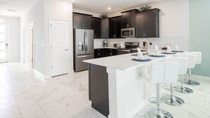 A modern kitchen with dark cabinets, a large island, and a white countertop. - Champions Gate 8BR Villa-pool Game Room Theater (Davenport)