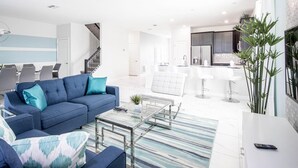 A modern living room with a blue sofa, a glass coffee table, and a striped rug. - Champions Gate 8BR Villa-pool Game Room Theater (Davenport)