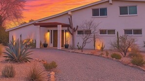 Una casa moderna con un jardín desértico, un patio cubierto y una vista despejada del cielo al atardecer.