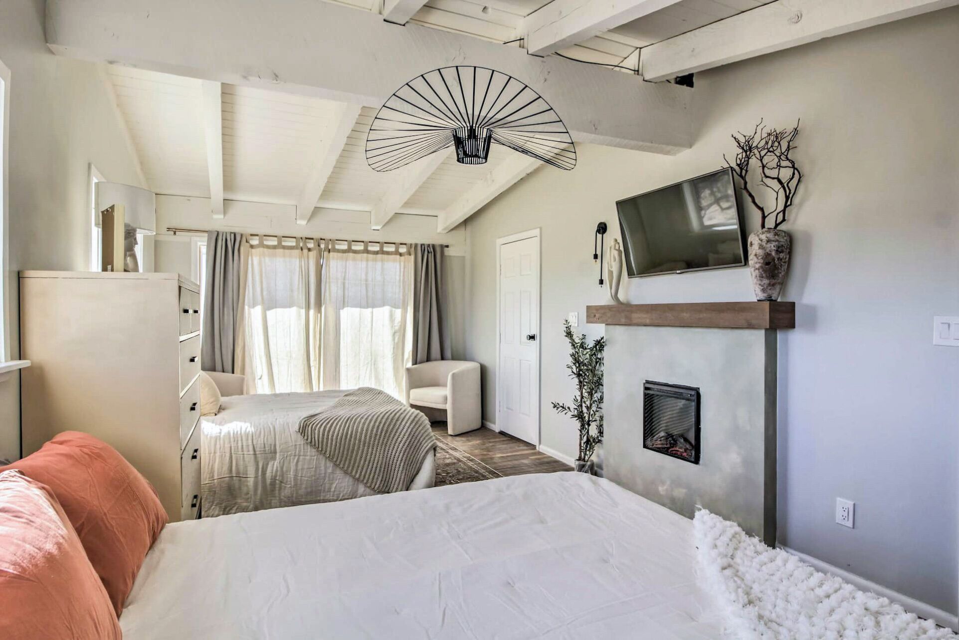 A bedroom with a bed, a TV, a fireplace, and a large window with curtains.