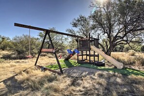 A wooden swing set and slide in a grassy outdoor area with trees in the background. - Newly renovated pool at the Modern Western Villa! (Tucson)