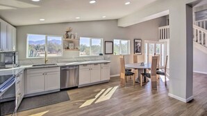 Una cocina moderna con armarios blancos, lavavajillas y un comedor con sillas y una mesa de madera.