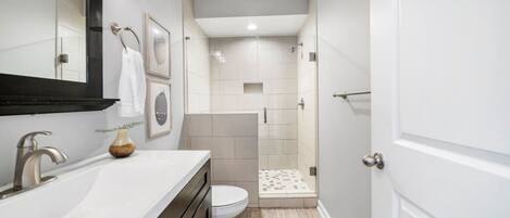 Un baño moderno con un lavabo blanco, un mueble de madera oscura y un espejo grande.