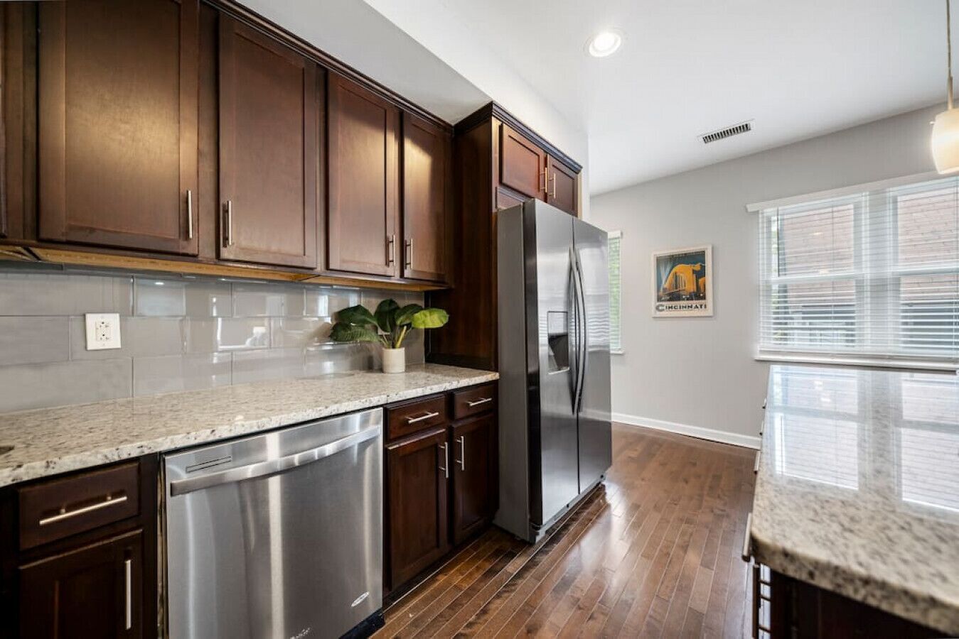 A kitchen with dark wooden cabinets, stainless steel appliances, a granite countertop, and a potted plant.