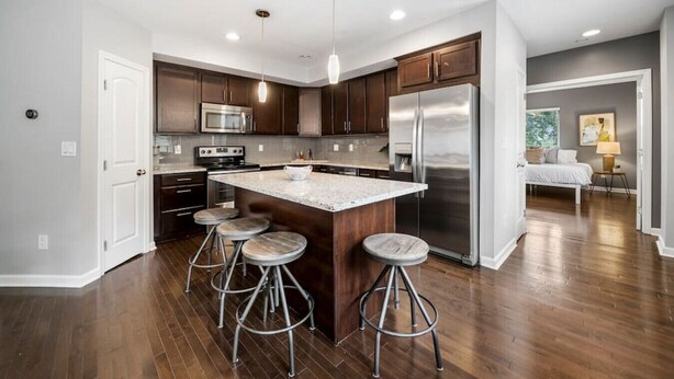 A modern kitchen with dark wood cabinets, stainless steel appliances, and a central island with stools. - Stylish 2BR near City Center | OTR, UC, Zoo (Cincinnati)