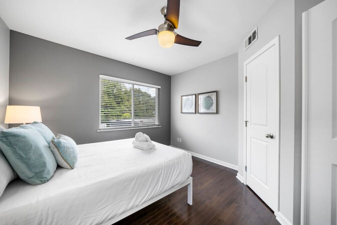 A bedroom with a bed, a ceiling fan, a window with blinds, and a door.