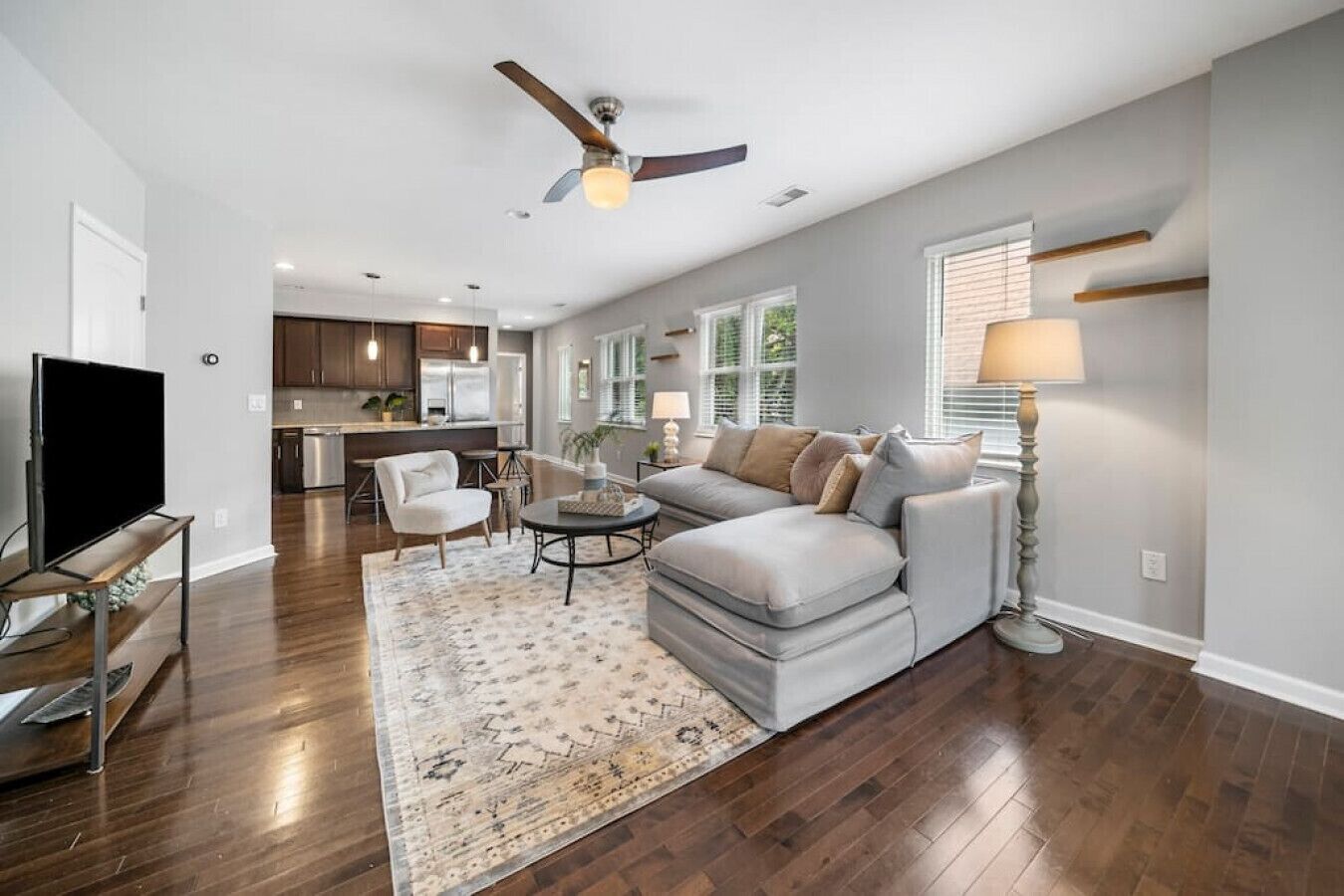 A spacious living room with a grey sectional sofa, a flat-screen TV, and a ceiling fan.