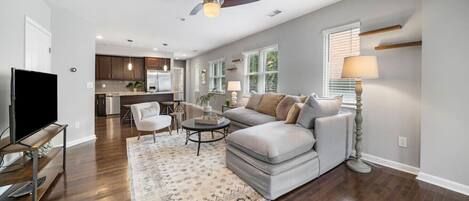 A spacious living room with a grey sectional sofa, a flat-screen TV, and a ceiling fan.