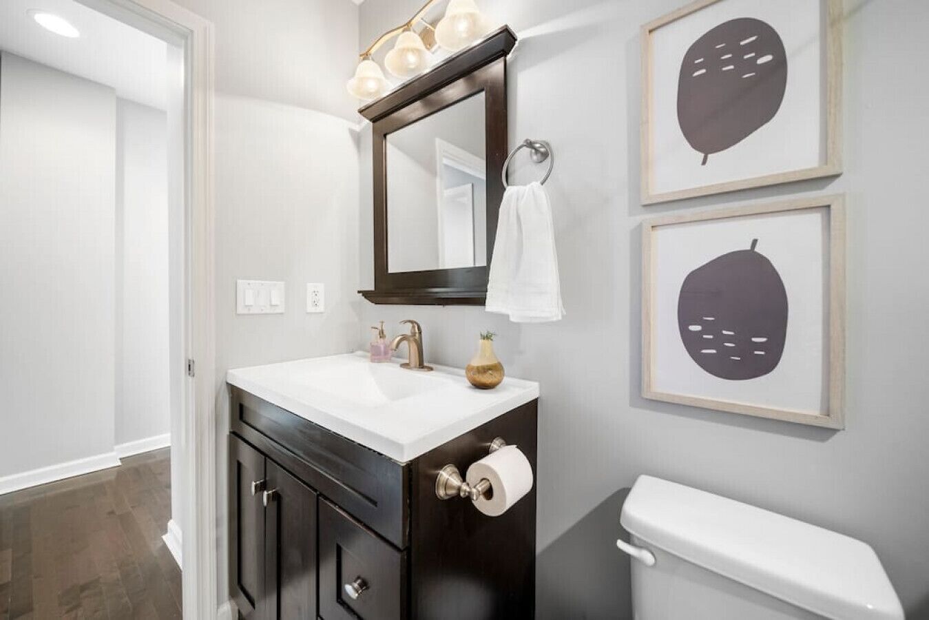 A bathroom with a white sink, dark wooden vanity, a mirror, and two framed wall art pieces.