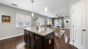 A spacious kitchen with a central island, dark wood cabinets, and a large window with blinds. - Stylish 2BR near City Center | OTR, UC, Zoo (Cincinnati)