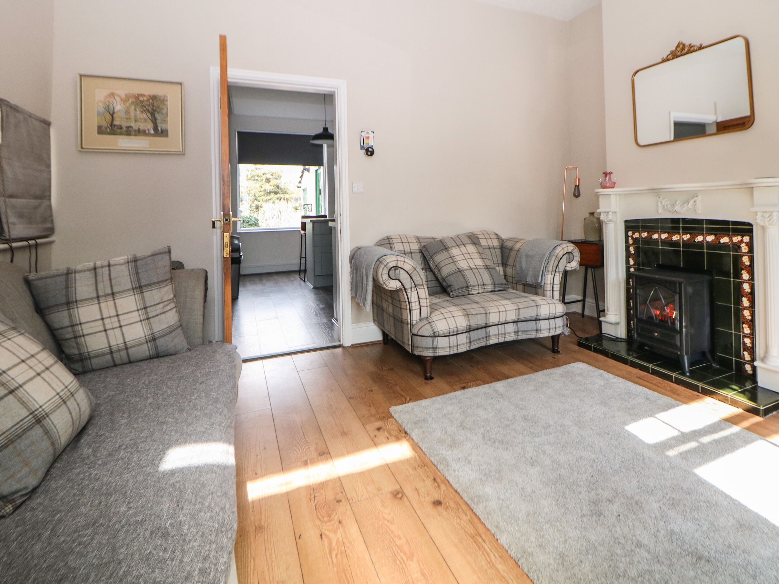 A living room with a fireplace, a sofa set, and a door leading to a kitchen.