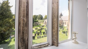 Une vue sur un cimetière, avec ses pierres tombales et une église, à travers une fenêtre à cadre en bois.