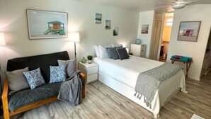 Ett sovrum med en säng, en soffa, ett nattduksbord med en lampa och ett litet bord med en växt.