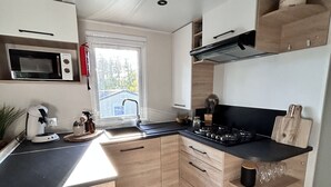 Uma cozinha moderna com armários de madeira, micro-ondas embutido, fogão a gás e janela que permite entrada de luz natural.