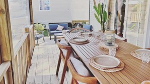 Uma área de refeições ao ar livre com uma mesa de madeira posta para quatro pessoas, rodeada por cadeiras de vime.