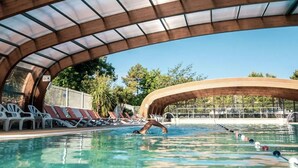 Piscina com estrutura de teto curva, espreguiçadeiras e céu azul ao fundo.