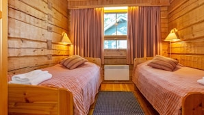 A cabin with two wooden beds, a window with curtains, and a small heater between the beds.