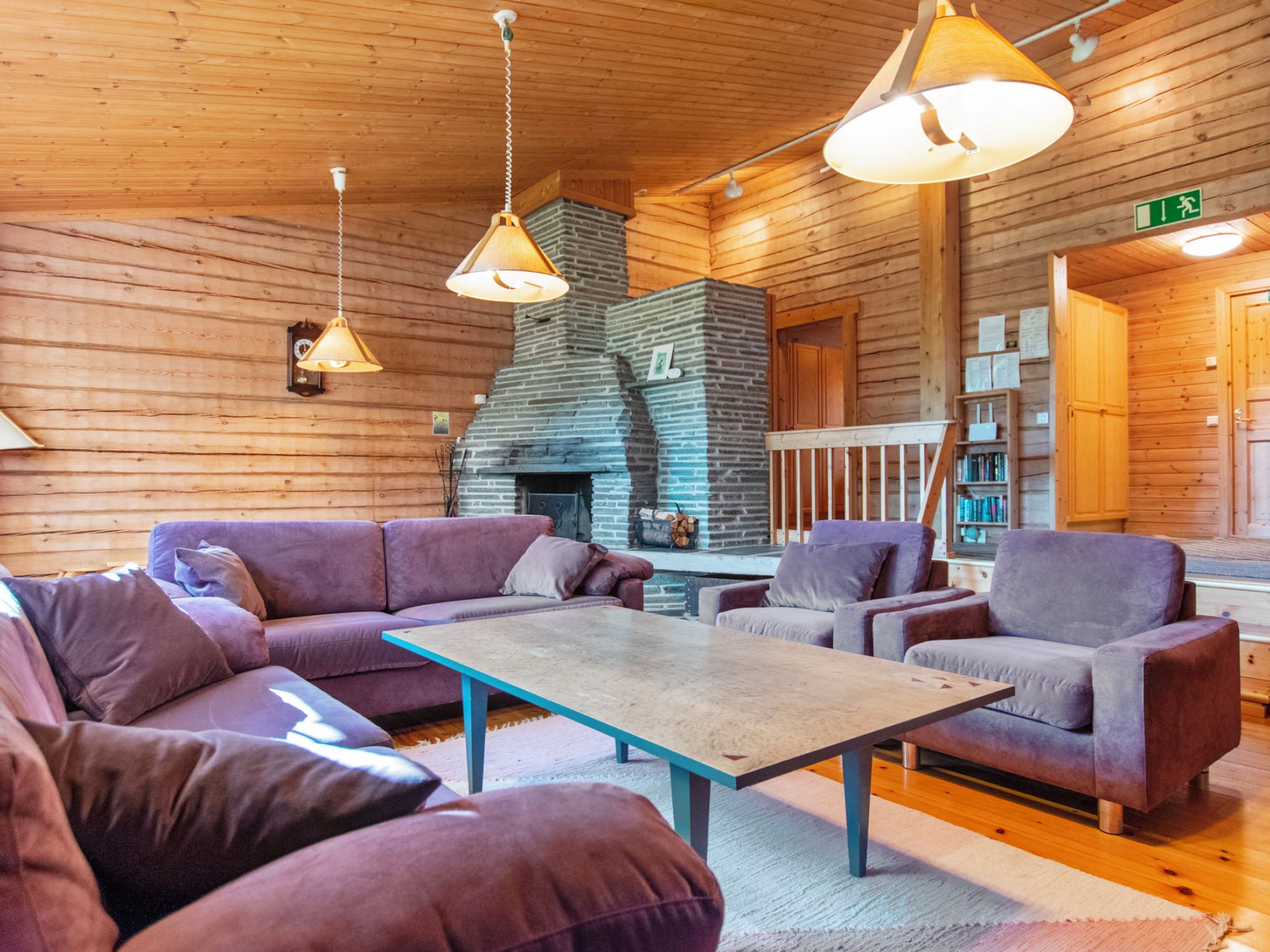 A cozy log cabin interior with a fireplace, wooden walls, and purple furniture.