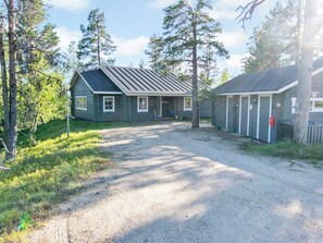 En toetages hytte med grusvej, der fører til indgangen, omgivet af træer.