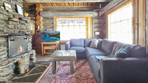 A cozy log cabin interior with a stone fireplace, a sofa, and a large window.