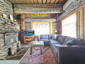 Ein rustikales Blockhaus-Interieur mit Kamin aus Stein, einer Couch, einem Couchtisch und einem großen Fenster.