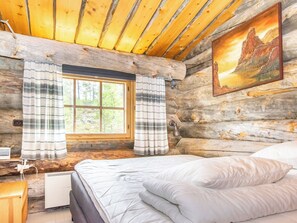 Ein Holzchalet-Innenraum mit Bett, einem Fenster mit Vorhängen, einem Gemälde an der Wand und einer Holzzahl.