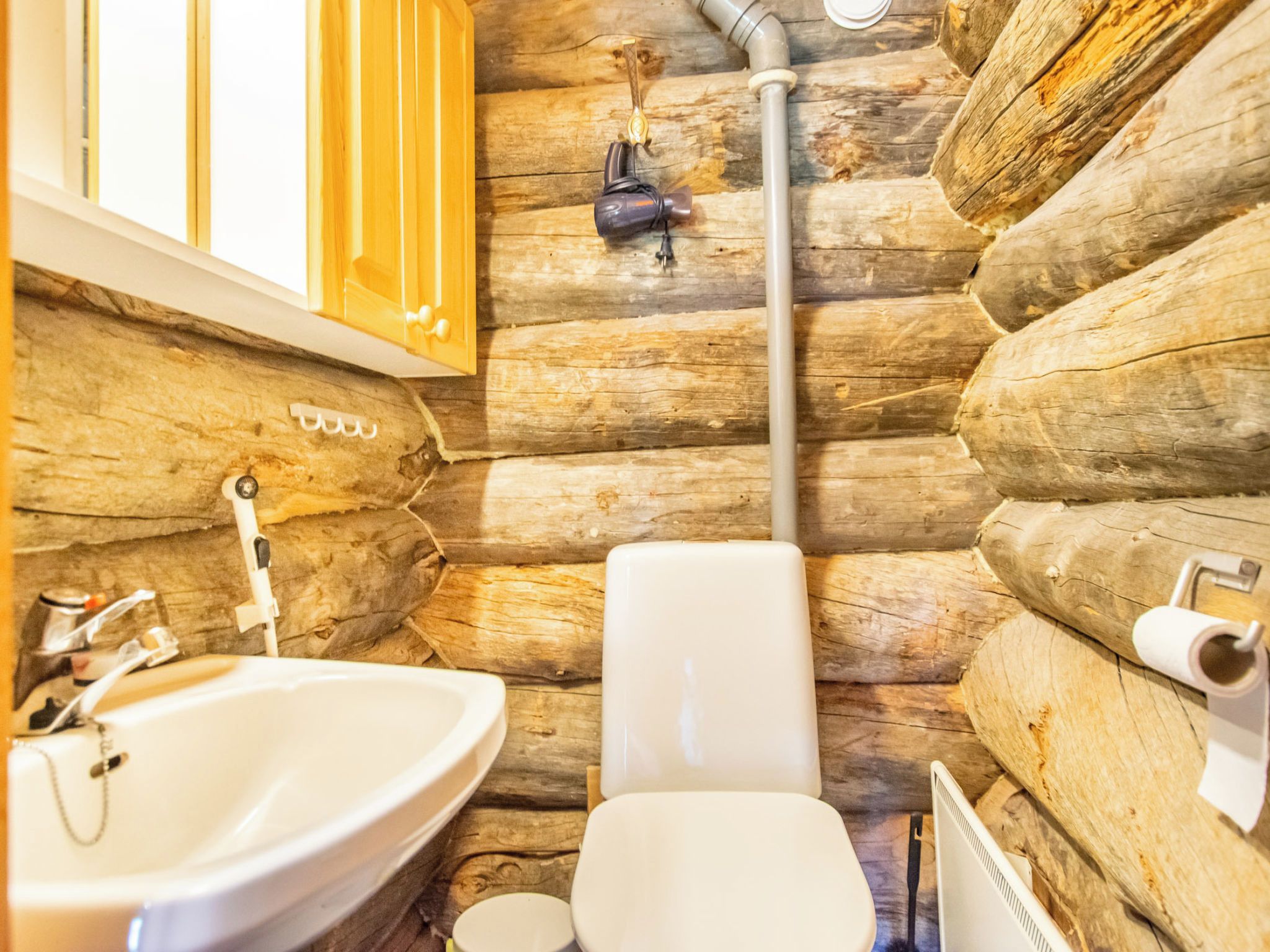 A rustic cabin-style bathroom with a wooden log wall, a white sink, and a toilet.