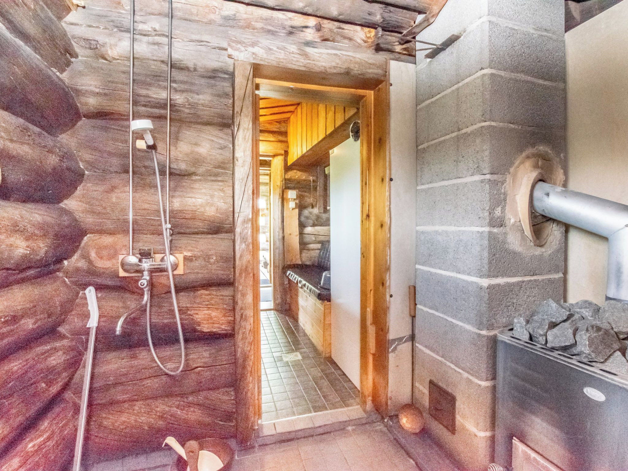 A log cabin interior with a wooden shower, a stone wall, and a fireplace.