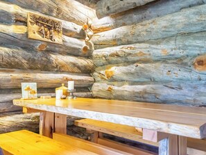 A rustic wooden cabin interior with a wooden bench and table, a framed picture on the wall, and a candle holder.