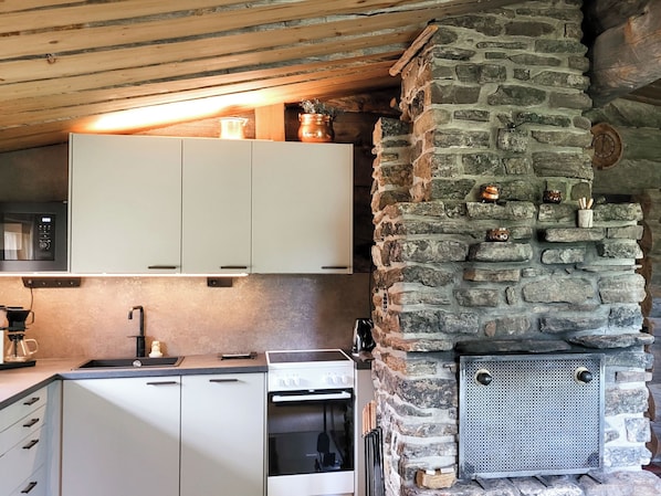 Une cuisine avec des armoires blanches, un mur en pierre et une cuisinière encastrée.