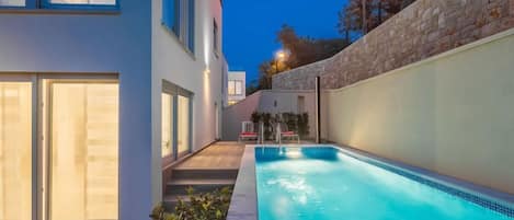 En modern byggnad med en swimmingpool, stora fönster och en stenmur.