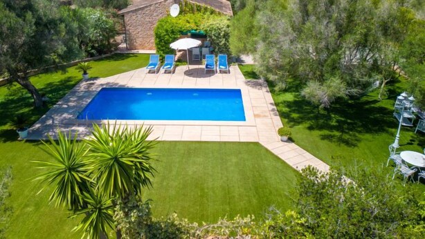 A rectangular swimming pool with a stone deck, surrounded by a well-manicured lawn and trees. - Sa Teulada by Interhome (Santa Margalida)