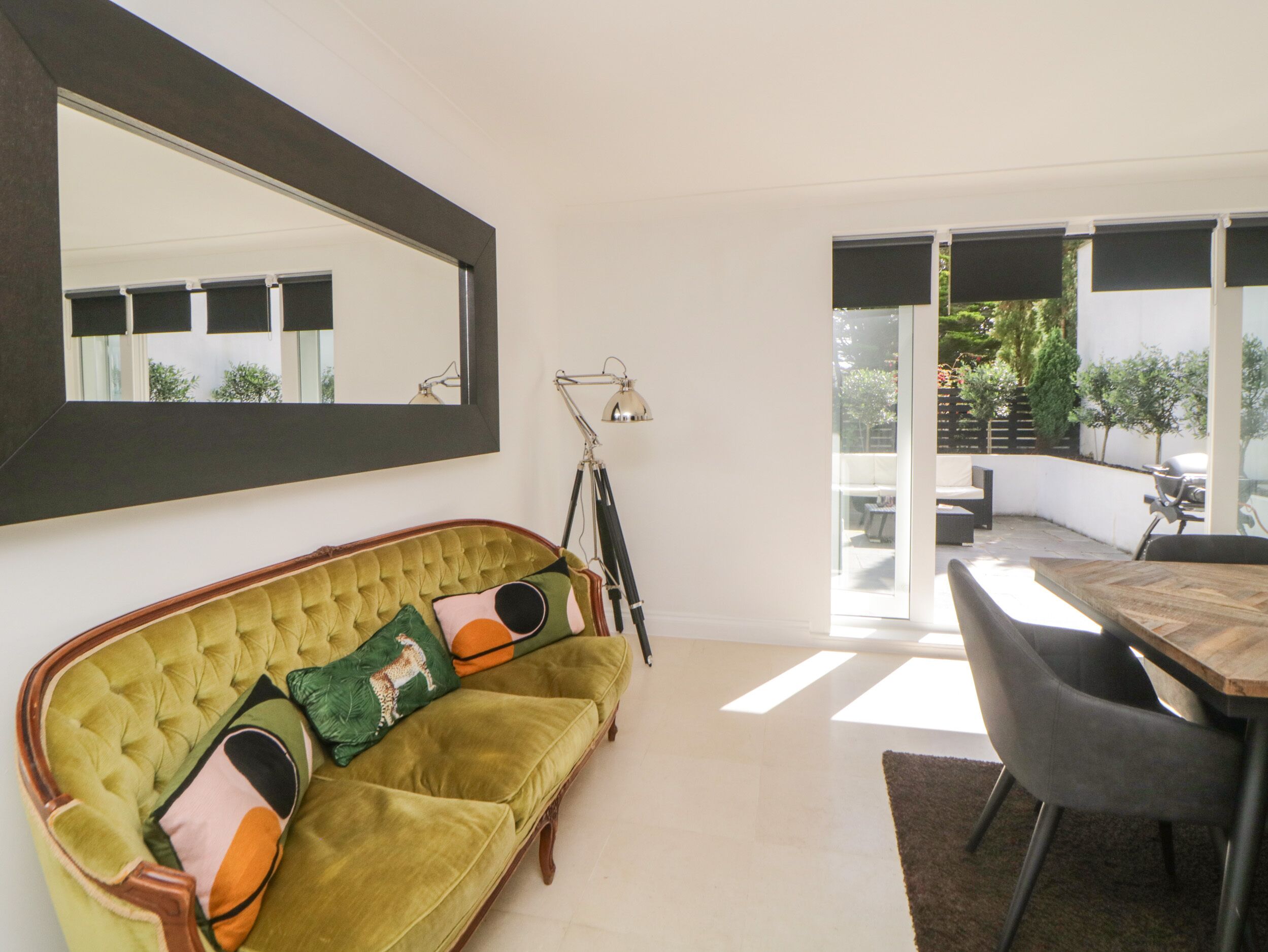 A modern living room with a green sofa, a wooden dining table, and a large mirror on the wall.