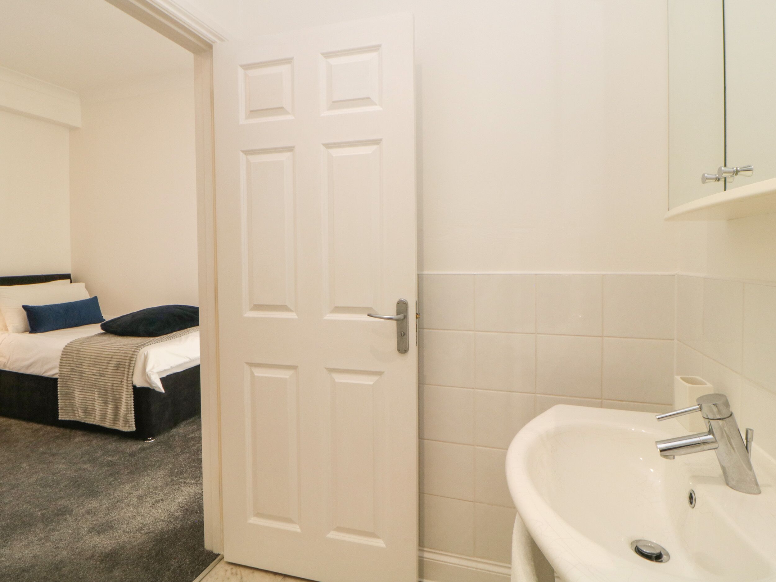 A hotel room with a bed, a white door, and a bathroom with a sink and mirror.