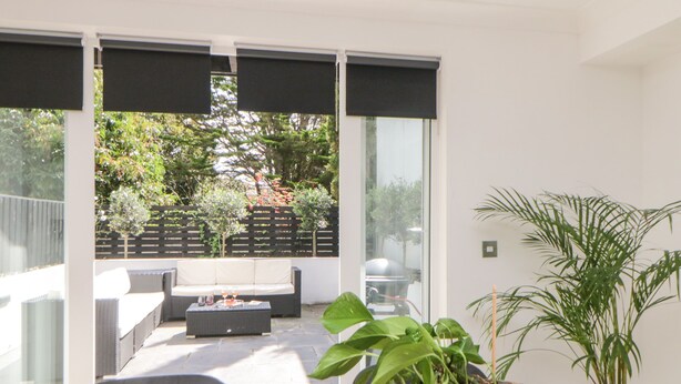 A modern outdoor seating area with a sofa and coffee table, a potted plant on the table, and a view of a garden through large glass doors.