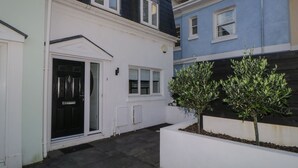 A two-story house with a black roof, white exterior walls, and a small front yard with two trees.