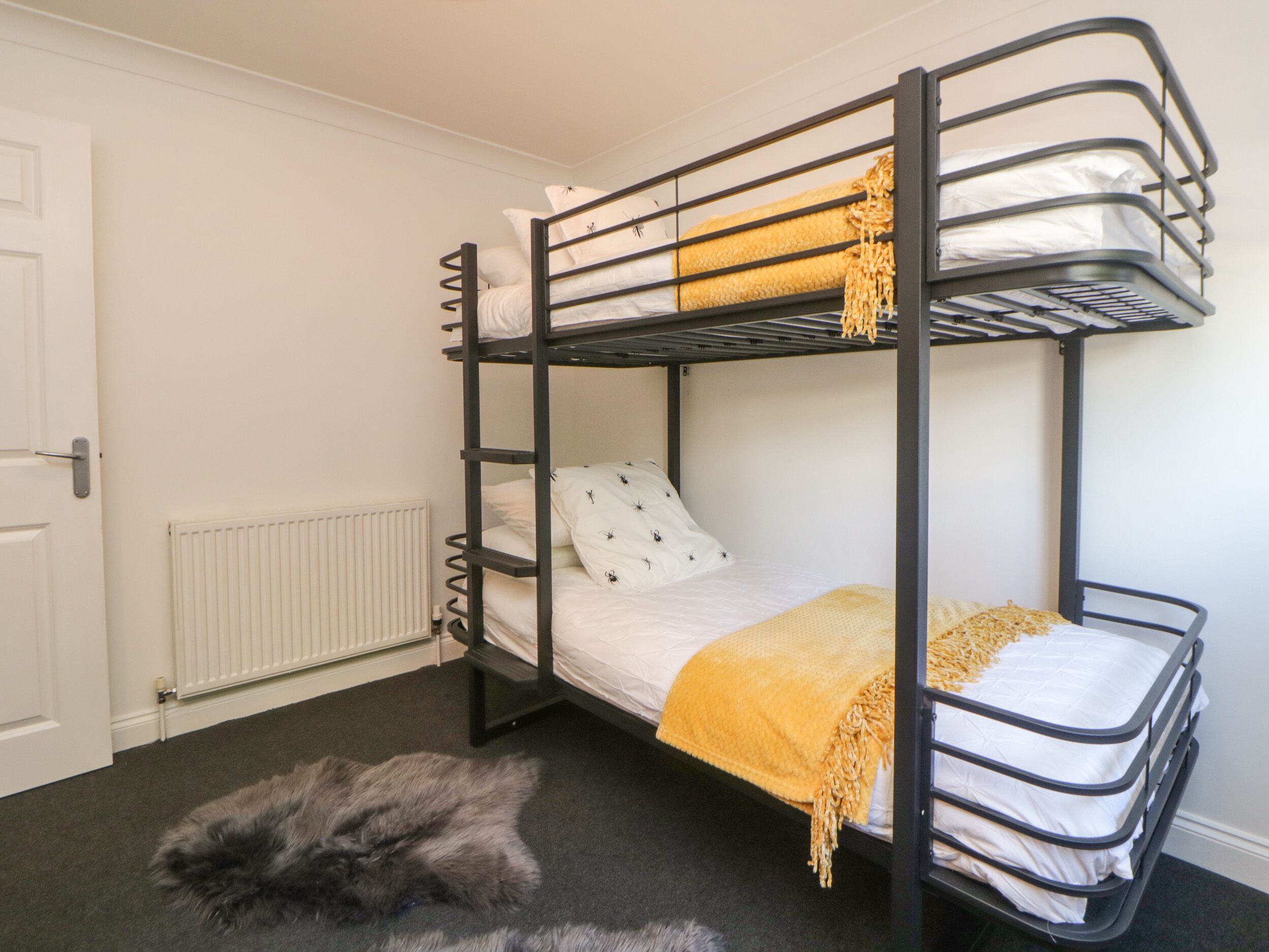 A bunk bed with two levels, a white door, a radiator, and a fluffy grey rug on the floor.