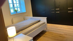 A bedroom with a bed, a bedside lamp, a window, and a black wardrobe.