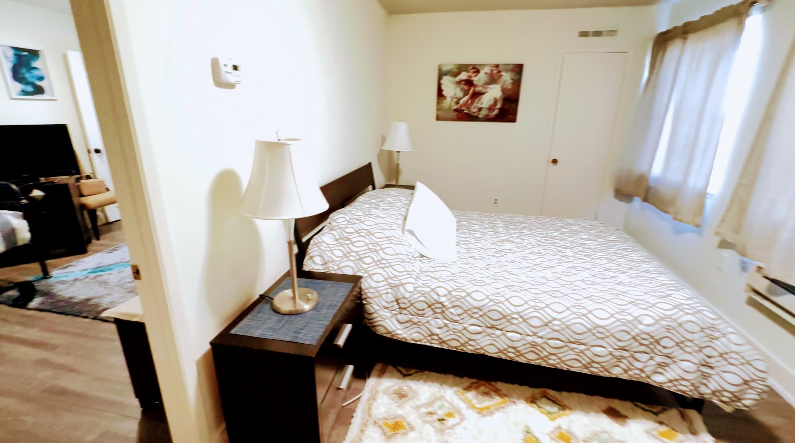 A hotel room with a bed, two bedside lamps, a painting on the wall, and a window with curtains.