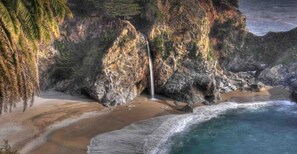 A beach with a waterfall, rocky cliffs, and ocean waves.